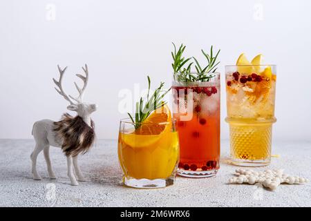 Drei farbenfrohe Weihnachtscocktails in Gläsern auf einem weißen Tisch. Auswahl an frischen Urlaubsgetränken. Rote Sangria-Cocktails, orange Stockfoto