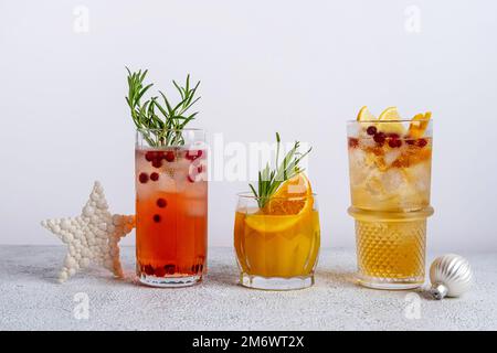 Drei farbenfrohe Weihnachtscocktails in Gläsern auf einem weißen Tisch. Auswahl an frischen Urlaubsgetränken. Rote Sangria-Cocktails, orange Stockfoto