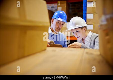 Das wird heute versendet. Ein Mann und eine Frau, die den Bestand in einem großen Vertriebslager inspizieren. Stockfoto