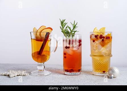 Drei farbenfrohe Weihnachtscocktails in Gläsern auf einem weißen Tisch. Auswahl an frischen Urlaubsgetränken. Rote Sangria-Cocktails, orange Stockfoto