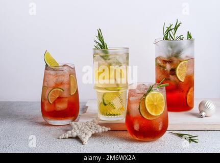 Vier farbenfrohe Weihnachtscocktails in Gläsern auf einem weißen Tisch. Auswahl an frischen Urlaubsgetränken. Erdbeermojito, Orangenpunsch Stockfoto