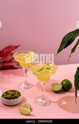 Margarita-Cocktail. Konzept klassischer Getränke. Erfrischende, farbenfrohe Sommergetränke auf pinkfarbenem Hintergrund mit Palmenblättern. Bar Stockfoto