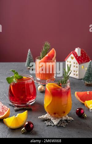 Drei festliche Cocktails mit verschiedenen Zitrusfrüchten. Auswahl an alkoholischen Weihnachtsgetränken. Rosa und rote Sangria-Cocktails, Granatapfel Stockfoto