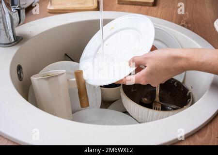 Frauenhände waschen den Teller unter fließendem Wasser. Dreckiges Geschirr im Waschbecken in der Küche, Chaos nach dem Mittagessen, zu faul, um di zu waschen Stockfoto