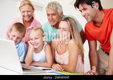 Ich habe ein paar Familienfotos durchsucht. Eine glückliche Familie, die sich über mehrere Generationen hinweg auf einem Notebook umsieht. Stockfoto