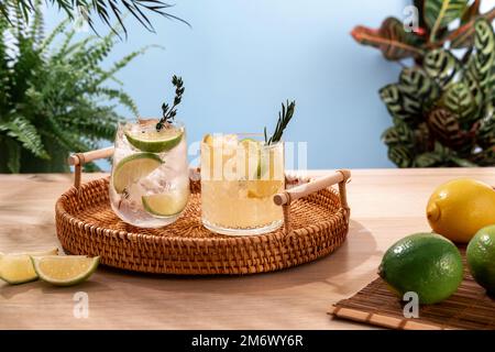 Glitzernde Cocktails mit Eis und Zitrusfrüchten auf einem Korbteller. Beliebte helle, erfrischende alkoholische Getränke. Erfrischende Sommergetränke. Stockfoto