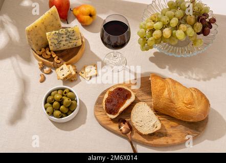 Glas Rotwein mit Trauben, Käse und Salami auf hellem Tischhintergrund. Rotwein mit Käse und Obst. Platz für Text Stockfoto