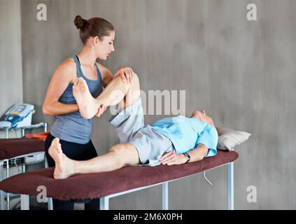 Ihre Patienten dabei zu unterstützen, stark und gesund zu bleiben. Eine Physiotherapeutin, die mit einem älteren Mann zusammenarbeitet. Stockfoto