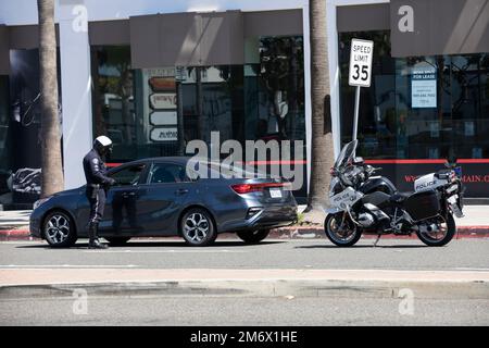 Costa Mesa, Kalifornien, USA - 20. März 2022: Ein Polizist mit Motorrad hält einen Autofahrer während einer Verkehrskontrolle an. Stockfoto
