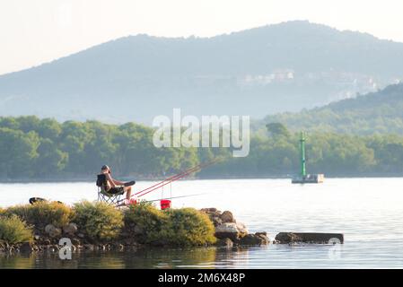 Der junge Mann sitzt und angelt auf dem Kanal sveti ante in sibenik kroatien Stockfoto