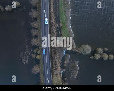 Die Autos fahren entlang der Straße, während sich das Welney Wash mit Überschwemmungen füllt, während die Pegel des Old Bedford River und des Flusses Delph nach kürzlichem Regen steigen, in Welney, Cambridgeshire, am 1. Januar 2023. Stockfoto