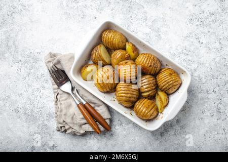 Hasselback Backkartoffeln in weißem Keramikauflauf auf weißem Betontischhintergrund Stockfoto