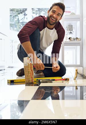 Dieses Heimwerkerprojekt Schritt für Schritt zu übernehmen. Porträt eines lächelnden Mannes, der Bodenfliesen legt. Stockfoto