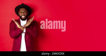 Angry Black Mann zeigt Kreuz, um etwas zu stoppen, suchen wütend und sinkende Angebot, in Party-Kleidung, roten Hintergrund Stockfoto