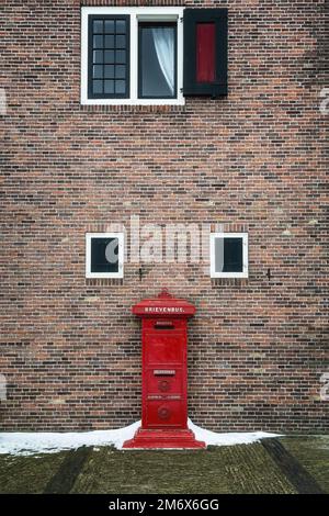 Zaandam, Niederlande, 10. Februar 2021: Altes rotes Postfach vor einer Ziegelwand in Zaanse Schans, Niederlande. Stockfoto