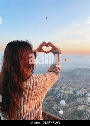 Glückliche Frau beim Sonnenaufgang und beobachtete Heißluftballons in Kappadokien, Türkei Stockfoto