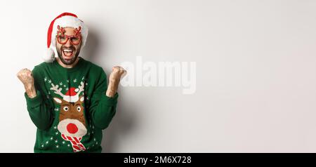 Weihnachtsfeiertage, Festungskonzept. Glücklicher Mann mit Weihnachtsmann-Hut triumphiert, trägt lustige Partybrille und freut sich, steht Stockfoto