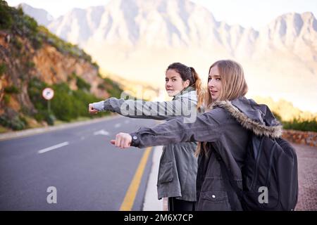 Ich warte auf eine Mitfahrgelegenheit. Ein kurzer Blick auf zwei junge Frauen, die per Anhalter auf einer Bergstraße trampen. Stockfoto