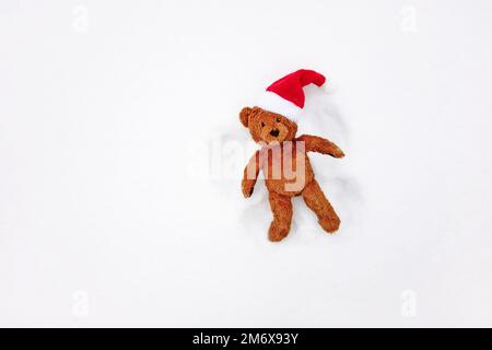 Schneeengel, Blick von oben - niedlicher Teddybär in rotem Weihnachtsmann hat Spaß in den Winterferien Stockfoto