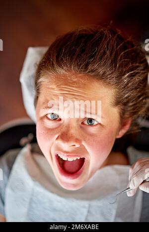 Auf dem gefürchteten Zahnarztstuhl. Hochwinkelaufnahme eines jungen Mädchens im Zahnarztstuhl, das verängstigt aussah. Stockfoto