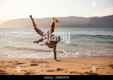 Seinen Breakdance zu veranstalten. Ein junger Mann, der am Strand tanzt. Stockfoto