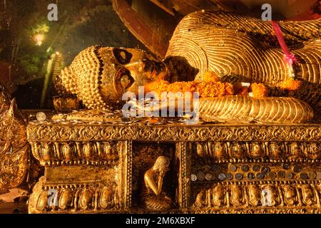 Liegender Buddha, bedeckt mit goldenen Blättern und Münzen im Sonnenlicht. Stockfoto