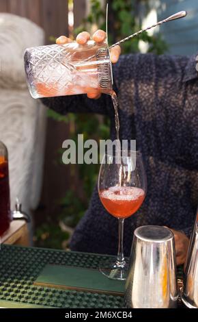 Gläser Cocktails an der Bar. Der Barkeeper schenkt ein Glas Sekt mit rotem Alkohol ein. Stockfoto