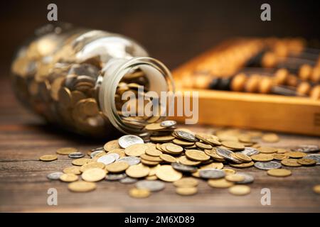 Glasbehälter mit goldenen Münzen und Abakus auf Holzhintergrund. Stockfoto