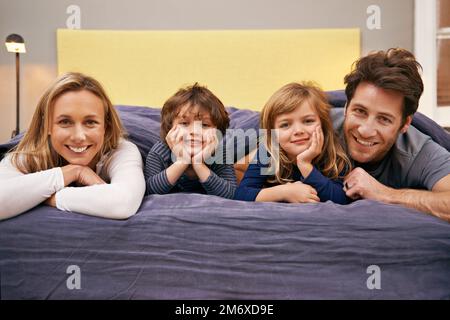 Sie sind eine enge Familie. Porträt einer jungen Familie, die nebeneinander auf einem Bett liegt. Stockfoto