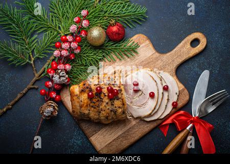 Weihnachtlich gebackener Schinken in Scheiben mit roten Beeren und festlichen Dekorationen Stockfoto