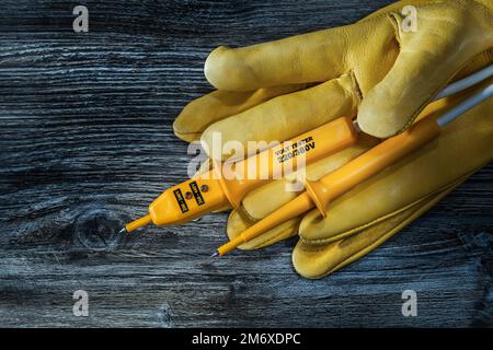 Sicherheitshandschuhe für Elektrotester auf altem Holzbrett. Stockfoto