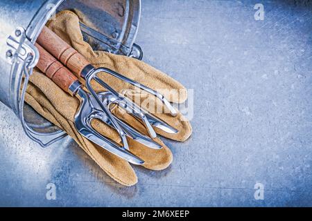 Verzinkter Eimer Metallrechen Gabel Lederschutzhandschuhe auf metallischem Hintergrund Gartenkonzept. Stockfoto