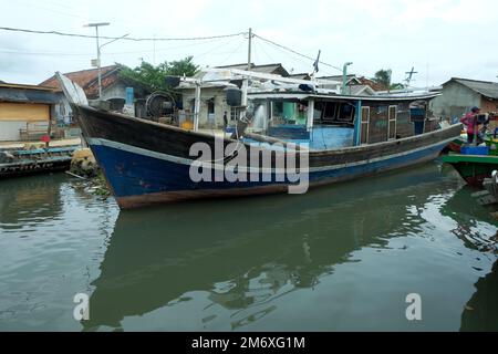 Lampung, Indonesien, 9. November 2022: Reihen von Fischerbooten auf dem Pier mit Schattenreflexionen im Wasser vor einem klaren Himmelshintergrund Stockfoto