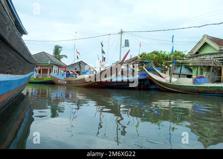 Lampung, Indonesien, 9. November 2022: Reihen von Fischerbooten auf dem Pier mit Schattenreflexionen im Wasser vor einem klaren Himmelshintergrund Stockfoto