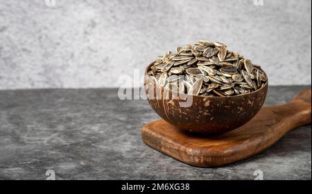 Geschälte Sonnenblumenkerne auf dunklem Hintergrund. Gesalzene Sonnenblumenkerne in einer Kokosnussschale. Speicherplatz kopieren Stockfoto