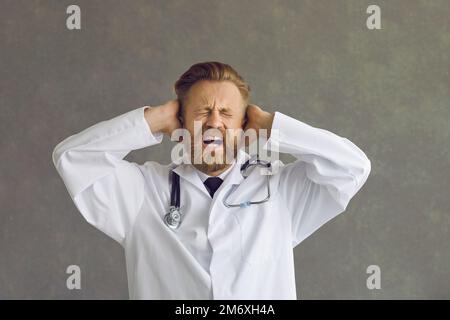 Frustrierter Mann, der schreit, die Augen geschlossen hält und die Ohren mit den Händen bedeckt Stockfoto