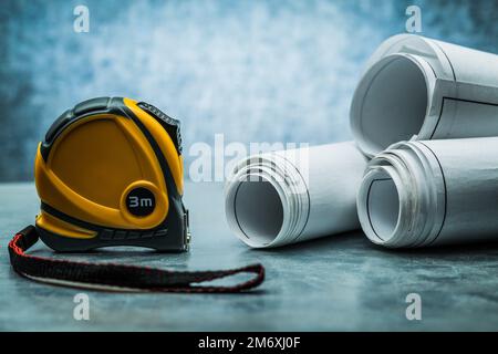 Bauroulette und gerollte Baupläne auf metallischem Hintergrund Stockfoto