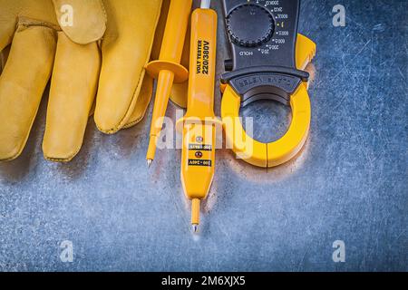 Sicherheitshandschuhe für elektrische Tester mit digitalem Amperemeter auf metallischem Oberflächenstromkonzept. Stockfoto