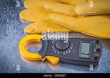 Schutzhandschuhe für digitale Amperemeter auf metallischem Hintergrund. Stockfoto