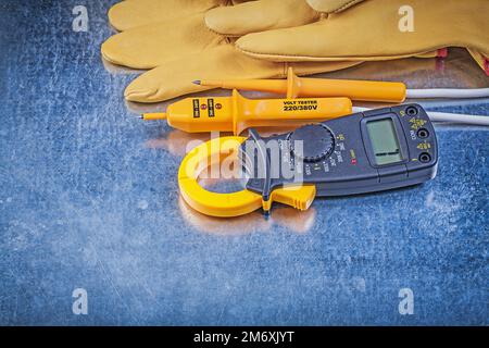 Sicherheitshandschuhe für digitale Strommesszangen für elektrische Tester im metallischen Hintergrund Konzept. Stockfoto