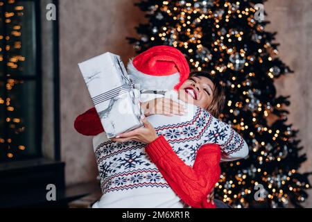 Ein junges glückliches Paar in festlicher Kleidung lächelt und umarmt sich nach dem Austausch von Weihnachtsgeschenken in festlicher Atmosphäre Stockfoto