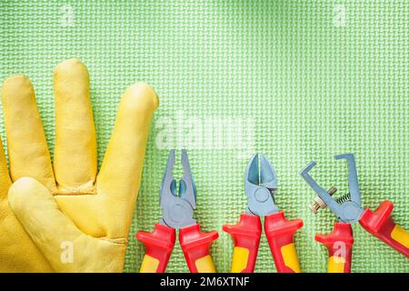 Zusammensetzung von Lederschutzhandschuhen Isolationsabisolierer Zange auf grünem Hintergrund Stromkonzept. Stockfoto