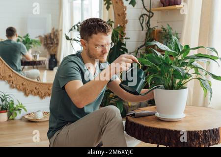 Mann, der zu Hause Pflanzen aus einer Gießkanne gießt. Hausarbeit- und Pflegepflanzenkonzept Stockfoto