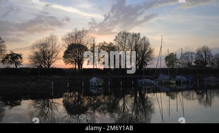 Reflexion von Bäumen im Wasser bei Sonnenuntergang im kleinen Hafen am Bodensee in der Nähe von Bregenz mit Rutsche vom Swimmingpool im Hintergrund Stockfoto