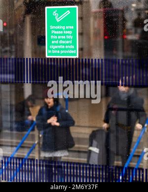 Schild an der Glaswand der Victoria Station, London, zeigt einen Raucherbereich an Stockfoto