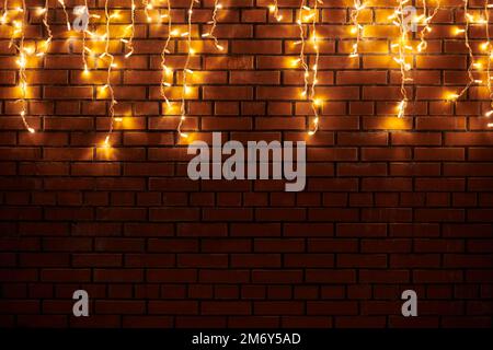 An der roten Backsteinwand hängen abends gelbe Girlanden, wunderschöne weihnachtsdekoration mit zauberhafter Feiertagsatmosphäre. Festliche Weihnachten g Stockfoto