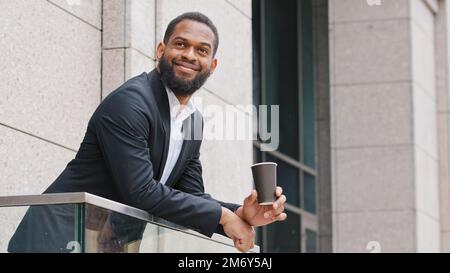Lächelnd entspannt afroamerikanische Firma Mitarbeiter Firma CEO Büro Manager Unternehmer Unternehmer ethnischer Mann mit dem man auf dem Balkon steht Stockfoto