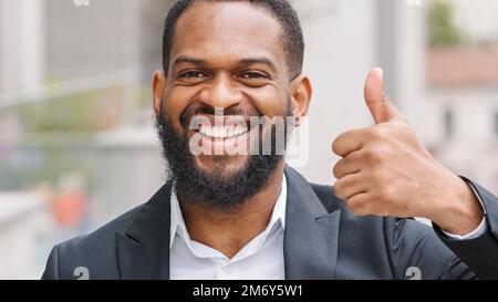 Millennials mit Bart, fröhlich lächelnd, männlicher afroamerikanischer Geschäftsmann, Boss, Unternehmer, Arbeitgeber, der Daumen nach oben zeigt, zeigen Zufriedenheit Stockfoto