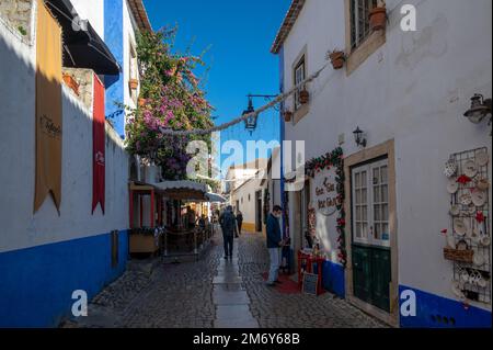 Blick auf die engen kopfsteingepflasterten Straßen des Obidos Viertels mit bunten Häusern, winzigen Geschäften und Cafés, die zu Weihnachten dekoriert sind. Stockfoto