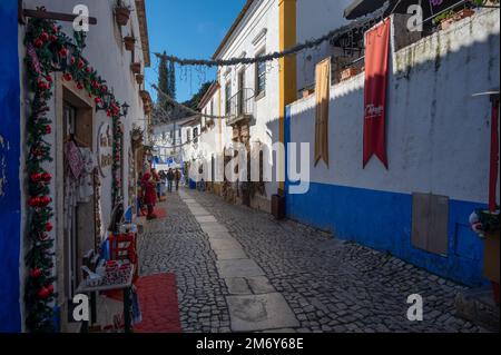 Blick auf die engen kopfsteingepflasterten Straßen des Obidos Viertels mit bunten Häusern, winzigen Geschäften und Cafés, die zu Weihnachten dekoriert sind. Stockfoto